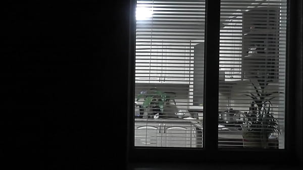 Peeping. Voyeur. Neighbor pervert voyeur in evening on street looks out window as naked sexy neighbor in kitchen prepares dinner for her husband. Naked in public. Naked at home. Family.  Outdoor